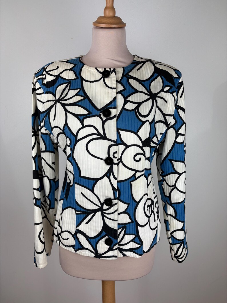 Puede incluir: Una chaqueta de botones con estampado floral blanco y azul y mangas largas.