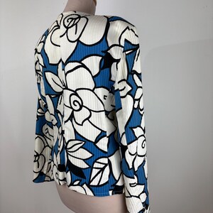 Puede incluir: Una blusa de manga larga blanca y azul con estampado floral. La blusa tiene una textura acanalada y un corte holgado.
