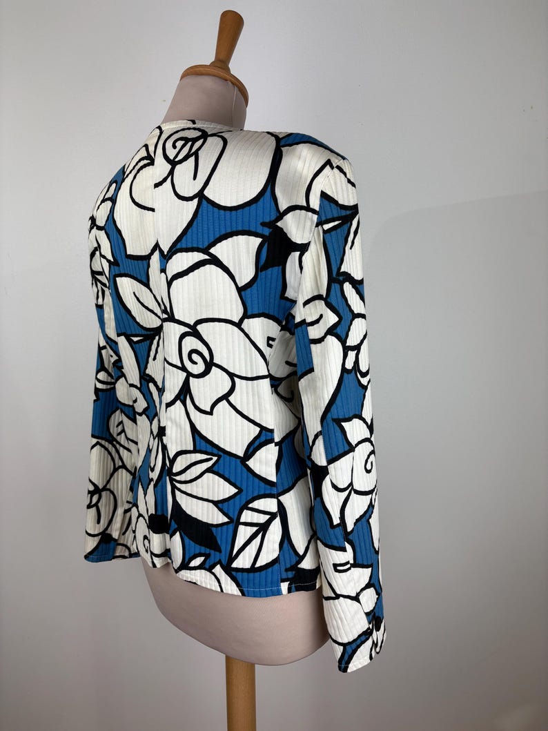 Puede incluir: Una blusa de manga larga blanca y azul con estampado floral. La blusa tiene una textura acanalada y un corte holgado.