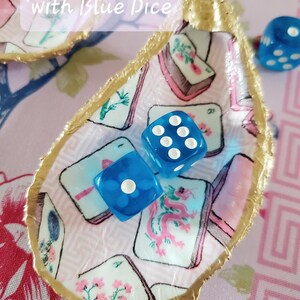 K&ouml;nnte beinhalten: Eine muschelf&ouml;rmige Schmuckschale mit goldfarbenem Rand und einem rosa-wei&szlig;en Muster. Zwei blaue W&uuml;rfel mit wei&szlig;en Punkten liegen darin. Der Text "with Blue Dice" ist sichtbar.