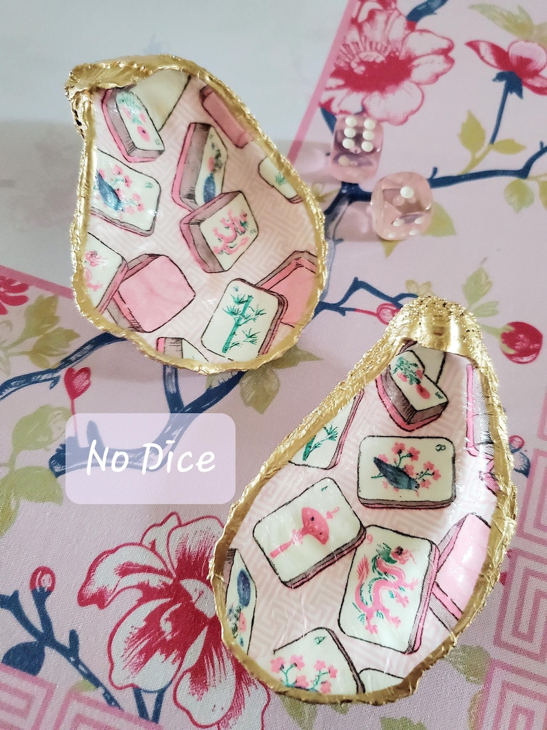 K&ouml;nnte beinhalten: Zwei dekorative Austernschalen mit goldfarbenen R&auml;ndern. Das Innere jeder Schale ist mit einem rosa Muster und Illustrationen von Mahjong-Steinen verziert. Der Text "No Dice" ist auf dem Bild sichtbar.