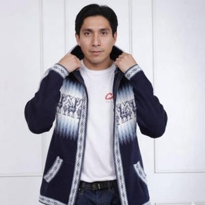 May include: A navy blue zip-up hooded sweater with a white and light blue geometric and llama pattern. The sweater has two front pockets and white trim. The person in the image is wearing a white t-shirt and blue jeans.
