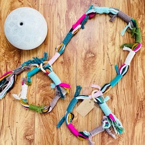 以下が含まれることがあります： タッセルが付いたカラフルなマクラメロープの壁掛けが2つ。大きい方は円形、小さい方は半円形。どちらもピンク、ブルー、グリーン、イエローなど様々な色でできています。