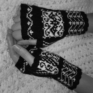 May include: A pair of black and white fingerless gloves with a geometric pattern. The gloves are made of a soft, knitted fabric.