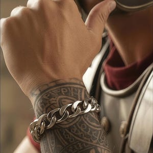 May include: A silver chain bracelet with large, interlocking links. The bracelet is worn on a tattooed arm, with intricate black ink designs. The arm is positioned near a Roman-style helmet and armor, suggesting a historical or warrior theme.