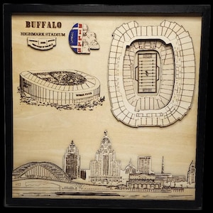 Può includere: Arte da parete in legno con raffigurazioni tagliate al laser di punti di riferimento di Buffalo, New York. Include uno stadio, un paesaggio urbano e il logo della squadra. L'opera d'arte è incorniciata in una cornice nera.