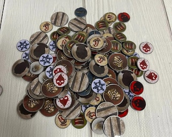May include: A pile of round, metal tokens with various designs, including skulls, snowflakes, and geometric patterns. The tokens are in shades of red, white, black, and brown.