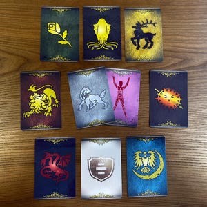 May include: A collection of ten rectangular cards with various illustrations. The cards feature images of a rose, squid, stag, lion, wolf, human figure, sun, dragon, shield, and eagle. Each card has a decorative border.