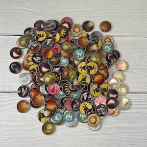 Peut inclure: Une collection de jetons ronds et colorés avec différents motifs, notamment des boucliers, des épées et d'autres symboles. Les jetons sont en métal et ont une finition brillante.