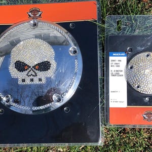 May include: Two Harley-Davidson derby covers and timer covers. The derby cover features a skull design made of rhinestones. The timer cover is also covered in rhinestones. Both are packaged in black and orange packaging.