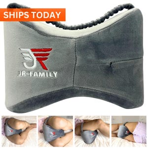 May include: Gray knee pillow with a zipper and a logo that says "JR-FAMILY". The pillow is shown being used by a person lying on their side with their legs elevated.