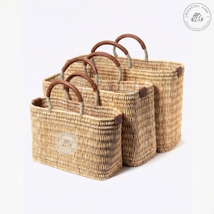 Peut inclure: Quatre paniers rectangulaires tress&eacute;s de diff&eacute;rentes tailles. Chaque panier a une poign&eacute;e en cuir marron et des coins renforc&eacute;s. Les paniers sont faits d'un mat&eacute;riau beige clair et sont dispos&eacute;s du plus petit au plus grand.