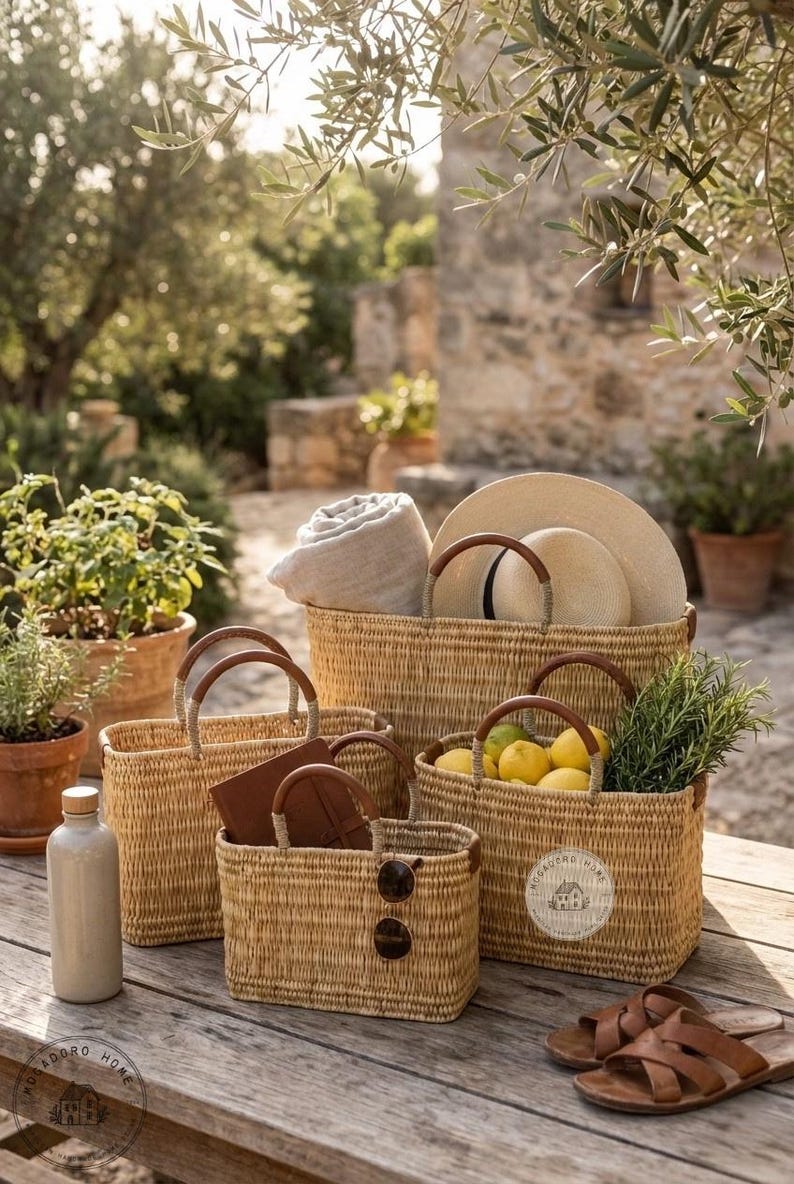 Peut inclure: Plusieurs paniers en paille tress&eacute;e de diff&eacute;rentes tailles, avec des poign&eacute;es en cuir marron, sont dispos&eacute;s sur une table en bois. Certains contiennent une couverture roul&eacute;e, des chapeaux, des citrons et des lunettes de soleil. Une bouteille et des sandales sont &eacute;galement pr&eacute;sentes.