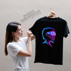 May include: Black t-shirt featuring a neon graphic of a person wearing futuristic eyewear. The design is in shades of blue, purple, and pink. The text "PIXEL UNIVERSE BY ZIAD" is printed on the top left of the shirt.