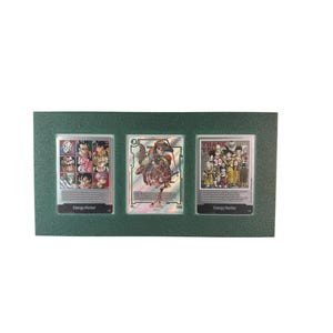 May include: A dark green framed display holding three trading cards. The cards feature colourful anime characters and text. The frame has a textured finish. Each card is displayed in a row with a silver border.
