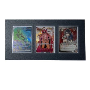 May include: Three trading cards displayed in a black frame. The cards feature colorful illustrations and Japanese text. The cards are protected by clear plastic sleeves. The cards are from the Pokemon and One Piece series.