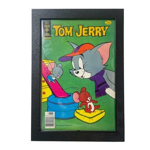 May include: Framed Tom and Jerry comic book cover. The cover features Tom the cat wearing a hat and scarf, looking at Jerry the mouse. The comic is in a black frame.