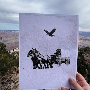 Könnte beinhalten: Eine Schwarzweißillustration eines Planwagens, der von zwei Pferden gezogen wird, mit einem Adler, der über ihnen fliegt. Das Bild ist auf weißem Papier gedruckt.