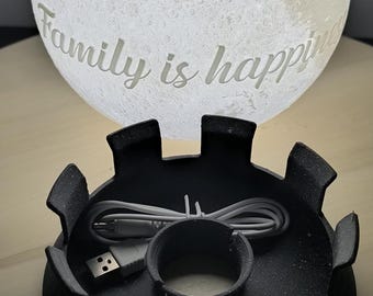 May include: A white moon lamp with the words "Family is happiness" inscribed on it. The lamp is sitting on a black base with a USB cable and a USB plug. The base has a circular opening in the center. The lamp is packaged in a clear plastic bag.