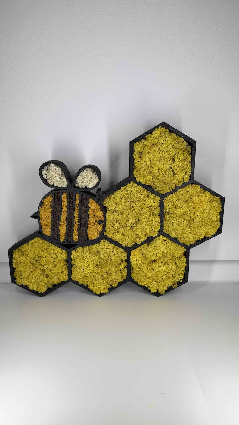 May include: A wall-mounted decorative piece featuring a black bee-shaped frame and five black hexagonal frames filled with bright yellow preserved moss. The bee has striped yellow and brown moss segments and two white moss-filled wings.