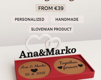 May include: A red wedding ring box with the names "Ana & Marko" in black. The box has two compartments with engraved text and a white heart design. The text "Wedding Ring Box", "Personalized", "Handmade", and "Slovenian Product" are also visible.