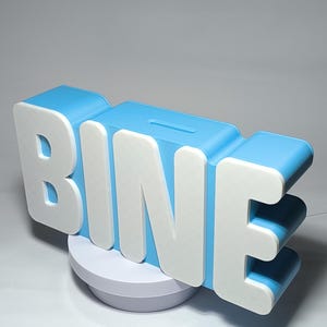 May include: A blue and white piggy bank in the shape of the word "BINE". The letters are white with a blue outline and a slot for inserting money. The bank sits on a white circular base.