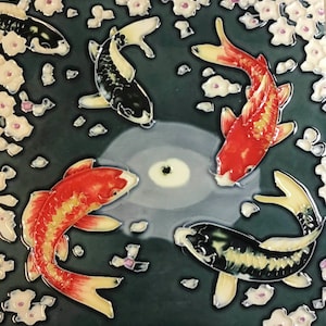 May include: Four koi fish swim in a pond with white flowers. Two of the fish are orange and two are black and white. The pond is a dark green colour.