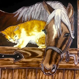 May include: A brown horse with a white mane and a brown leather halter looks out of a wooden stall. A small orange and white cat is curled up on the horse's back.