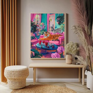 May include: A framed art print depicts a vibrant interior scene with a tiger and zebra lounging on a pink sofa. The artwork features a blue table with drinks, lush plants, and a colorful, tropical aesthetic.