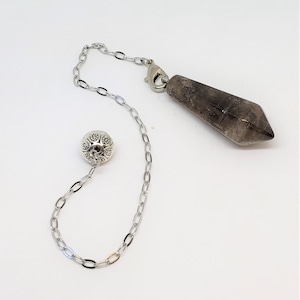 Könnte beinhalten: Eine silberne Kette mit einer silbernen Kugel an einem Ende und einem dunkelgrauen Kristallpendel am anderen Ende.