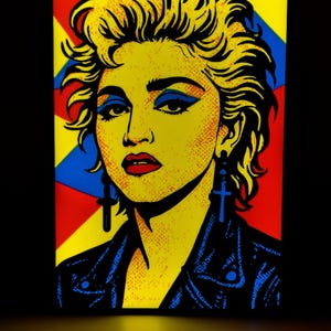 Op de afbeelding: Pop-art portret van een vrouw met geel haar, blauwe oogschaduw en rode lippenstift. Ze draagt een zwarte leren jas en blauwe kruisvormige oorbellen. De achtergrond heeft rode, gele en blauwe geometrische vormen.