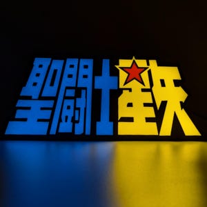 Op de afbeelding: Een oplichtend bord met Japanse karakters in blauw en geel, met een rode ster. Het bord is verlicht tegen een donkere achtergrond, wat een opvallend contrast creëert. Het ontwerp is waarschijnlijk voor een Japanse anime- of mangaserie.