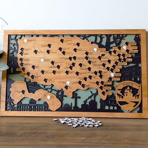 May include: A wooden map of the United States with black and white ghost icons marking haunted locations. The map is framed in wood and has a green background. The text "Haunted" is on a shield with a house and trees.