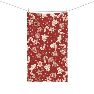 May include: A red and cream-colored Christmas-themed towel with a repeating pattern of gingerbread men, houses, stars, bells, and candy canes. The words "Fuck Trump" are printed on the towel.