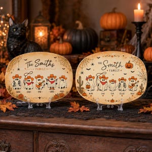May include: Two oval wooden plaques featuring a Halloween theme with ghost illustrations wearing cowboy hats. The left plaque reads The Smiths Family with names Mom, Dad, Eva, Luke, and Max. The right plaque reads The Smith Family with names Mom, Dad, Eva, Ellie, and Max.