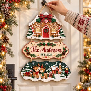 May include: A three-tiered wooden hanging sign featuring a gingerbread house top, a center plaque with the text The Andersons EST. 2026, and a bottom section depicting two reindeer in a snowy village scene with pine trees and a street lamp.