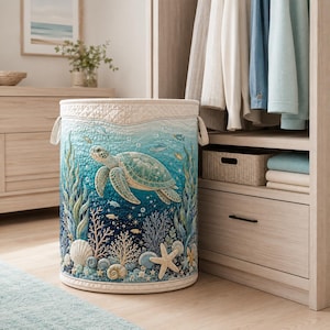 May include: A cylindrical fabric laundry hamper featuring a quilted texture and an ocean-themed print. The design displays a large sea turtle swimming among coral, seashells, and seaweed in shades of blue, teal, and white with two side handles.