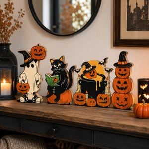 May include: A set of four Halloween-themed wooden tabletop decorations featuring a ghost holding a pumpkin, a black cat reading a book on a pumpkin, a cauldron with a pumpkin, and a stack of three jack-o'-lanterns, all in orange, black, and white.