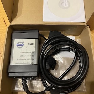 Peut inclure: Kit d'outil de diagnostic Volvo DiCE noir et argenté avec un CD-ROM, des câbles et un connecteur USB. L'outil comporte des indicateurs d'état pour le micrologiciel, l'USB, le Bluetooth et l'interface du véhicule. Le kit est dans une boîte en carton.