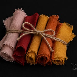 Op de afbeelding: Een bundel gekleurde linnen stofresten in roze, rood en geel-oranje, samengebonden met touw. De randen van de stof zijn gerafeld. De tekst "LinenPro 100% linen" is zichtbaar.