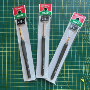 Peut inclure: Trois paquets d'aiguilles à crochet de la marque Tulip, chacun contenant une aiguille en or de 2,5 mm. Les paquets sont étiquetés "Tulip MinD 2,5 mm" et "4/0 2,50 mm Tulip".