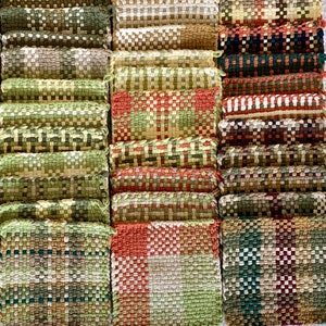 May include: A collection of square woven fabric coasters arranged in a grid. The coasters feature various plaid and checkered patterns in earthy tones including brown, tan, olive green, cream, rust orange, and dark forest green colors.