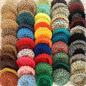 May include: A collection of handmade, crocheted coasters in various colors, including shades of brown, blue, red, green, and yellow. The coasters are arranged closely together, showcasing the texture and variety of the yarn used.