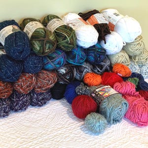 May include: A large assortment of yarn balls in various colors, including blue, green, orange, red, and pink. The yarn is arranged in a pile, with some balls still bearing labels. The image showcases a variety of textures and hues, perfect for knitting or crochet projects.