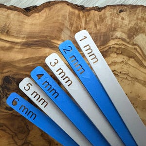 May include: Six white and blue plastic rulers with measurements in millimeters, ranging from 1 mm to 6 mm.