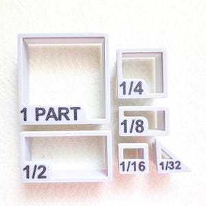 May include: White plastic fraction templates with black text. The templates are in various shapes, including squares, rectangles, and a triangle. The text includes fractions like 1/4, 1/8, 1/16, and 1/32, and the words "1 PART" and "1/2".