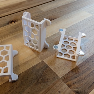 May include: Three white plastic organizers with a honeycomb pattern. The organizers are designed to hold small items and have a magnetic base.