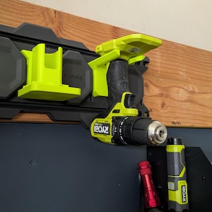 Può includere: Un trapano e una torcia elettrica neri e verdi sono montati su un organizzatore da parete nero e grigio. L'organizzatore ha un logo verde e nero che dice "Ryobi".
