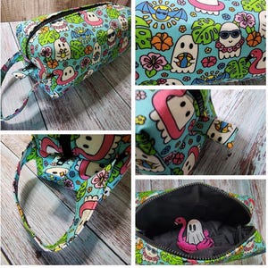 May include: A rectangular, zippered cosmetic bag with a colorful pattern of cartoon ghosts, flamingos, sunglasses, and tropical flowers on a light blue background. The bag has a black zipper and a matching handle.