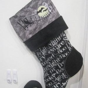 May include: Black and gray Christmas stocking with a silver glitter design featuring a moon, bats, and the text "Nightmare Before Christmas".